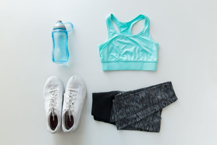 Flat lay of gym clothes, water bottle, white trainers, mint blue sports bra and grey leggings.